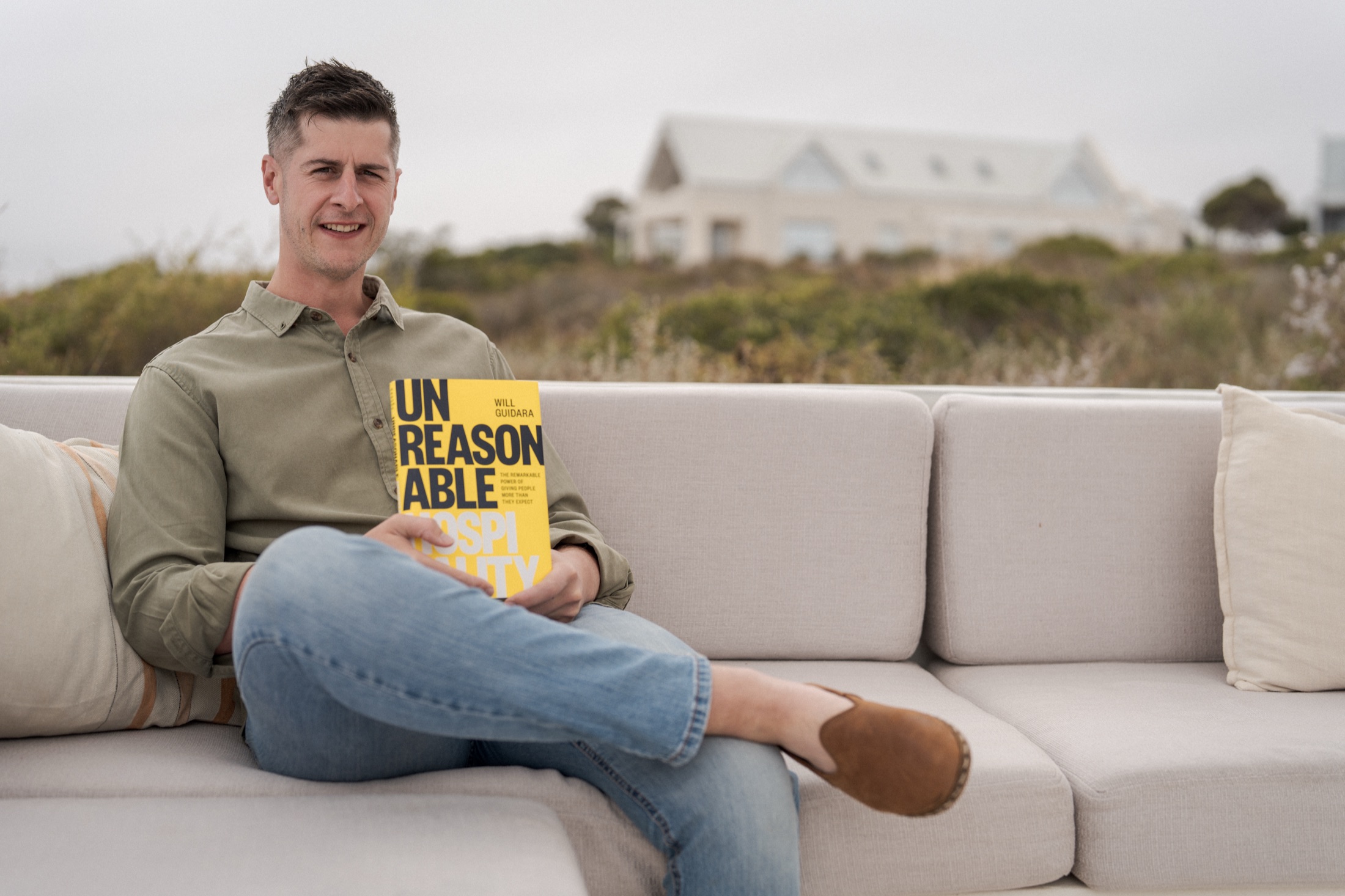 Matt Budden seated outdoors holding the book Unreasonable Hospitality